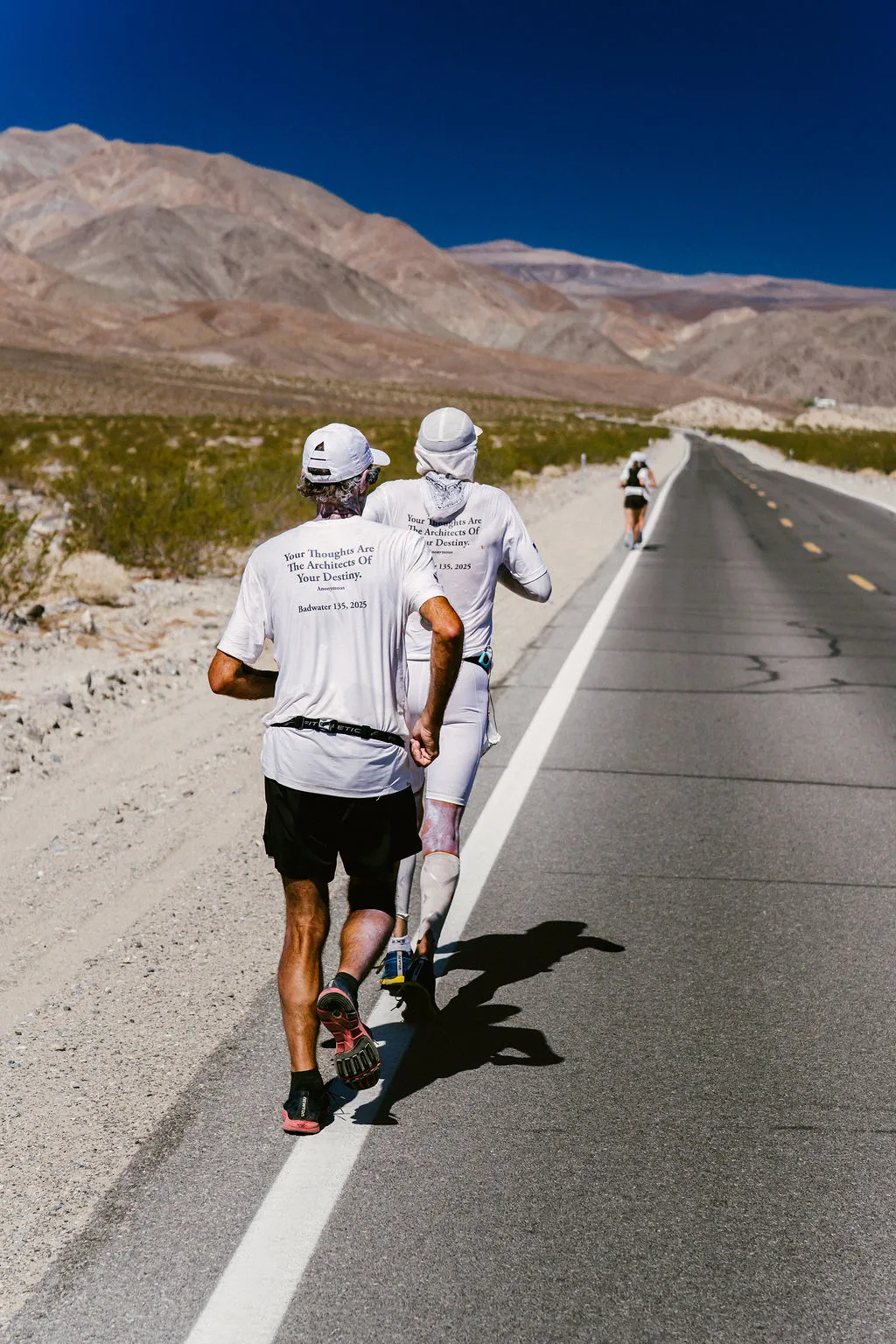Two runners on a Death Valley highway wearing shirts reading Your Thoughts Are The Architects Of Your Destiny