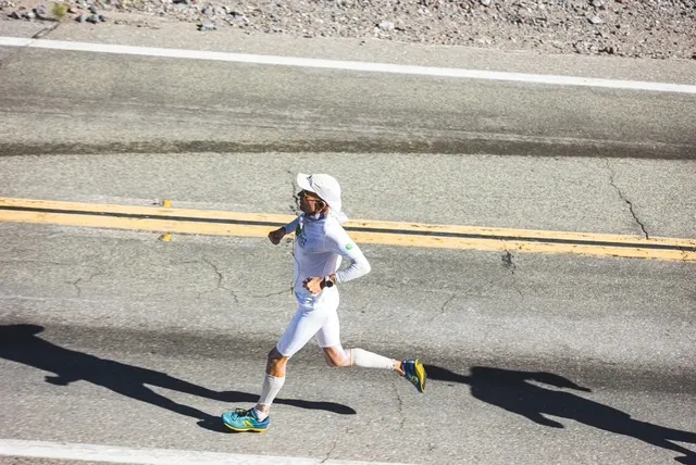 Harvey Lewis in white desert gear striding across a highway, seen from above
