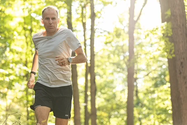 Harvey Lewis trail running along a sunlit woodland path during training
