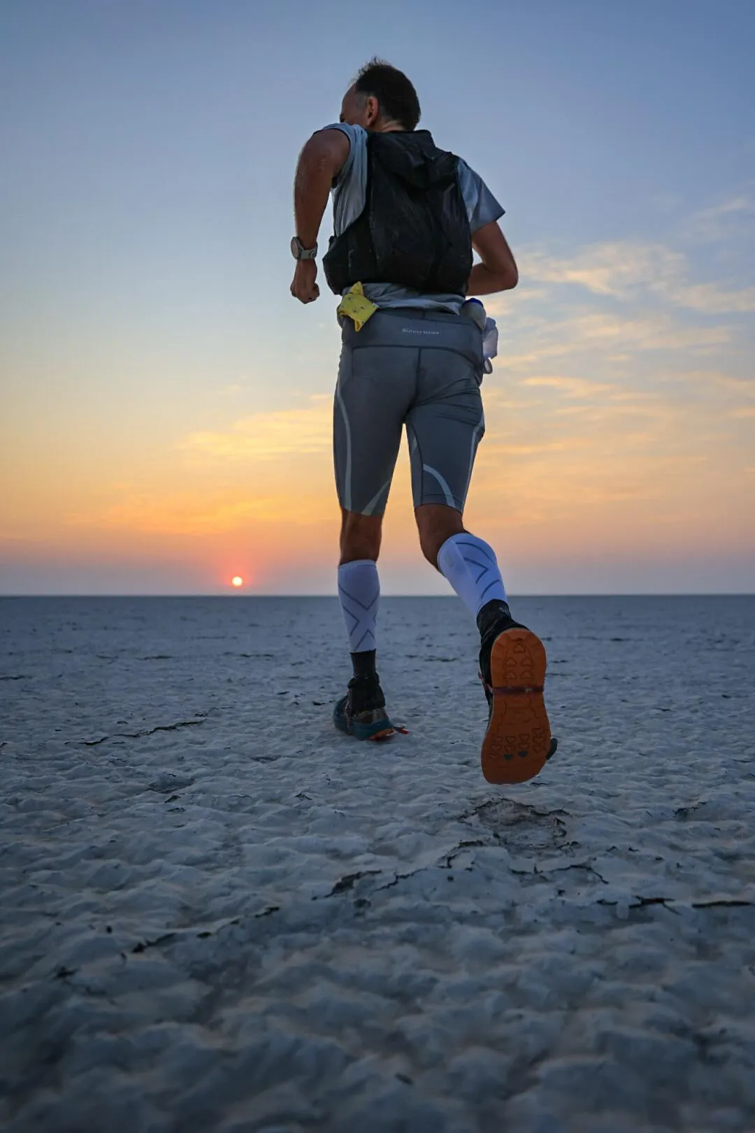 Harvey Lewis running alone across a salt flat toward the setting sun