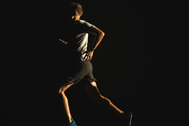 Harvey Lewis running in near-darkness, rim-lit by low sun